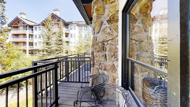 A balcony with a stone wall, a wooden deck, and a view of other buildings. - Top-Floor, Ski-In/Ski-Out Condo w/ Loft, Fireplace, Balcony & Shared Hot Tub (Steamboat Springs)