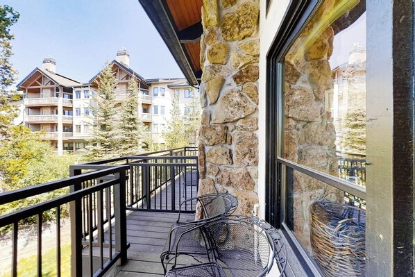 A balcony with a stone wall, a wooden deck, and a view of other buildings. - Top-Floor, Ski-In/Ski-Out Condo w/ Loft, Fireplace, Balcony & Shared Hot Tub (Steamboat Springs)