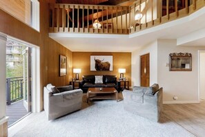 A spacious living area with a high ceiling, a wooden staircase, and a large window. - Lofty Ski-In/Ski-Out Condo w/ Fireplace, Balcony & Shared Hot Tub/Grill/Laundry (Steamboat Springs)