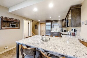 A kitchen with granite countertops, stainless steel appliances, and dark wood cabinetry. - Lofty Ski-In/Ski-Out Condo w/ Fireplace, Balcony & Shared Hot Tub/Grill/Laundry (Steamboat Springs)