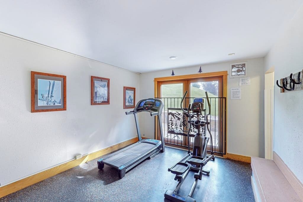 A gym with a treadmill, elliptical, and stationary bike, a door leading outside, and framed pictures on the wall.