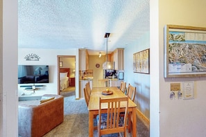 A room with a dining table, chairs, a sofa, a TV, and a kitchen area.