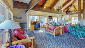 A spacious room with a high ceiling, wooden beams, a desk, a sofa, and a large plant.