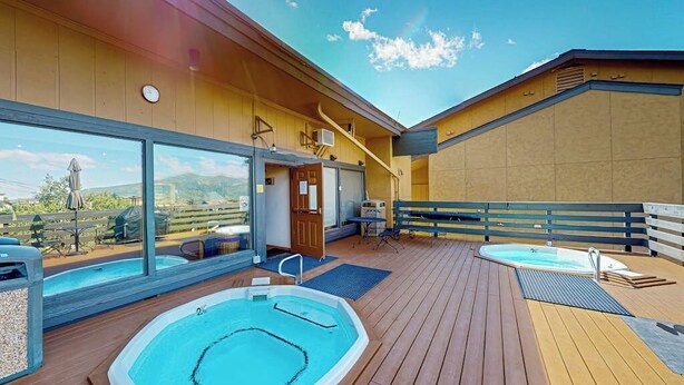 A rooftop deck with two hot tubs, a covered patio area, and a view of the surrounding landscape.