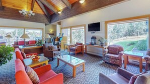 A spacious living area with a high ceiling, large windows, and a view of a golf course.