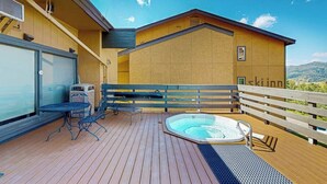 A wooden deck with a hot tub, outdoor seating, and a view of the mountains.