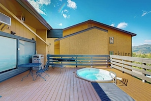 A wooden deck with a hot tub, outdoor seating, and a view of the mountains.
