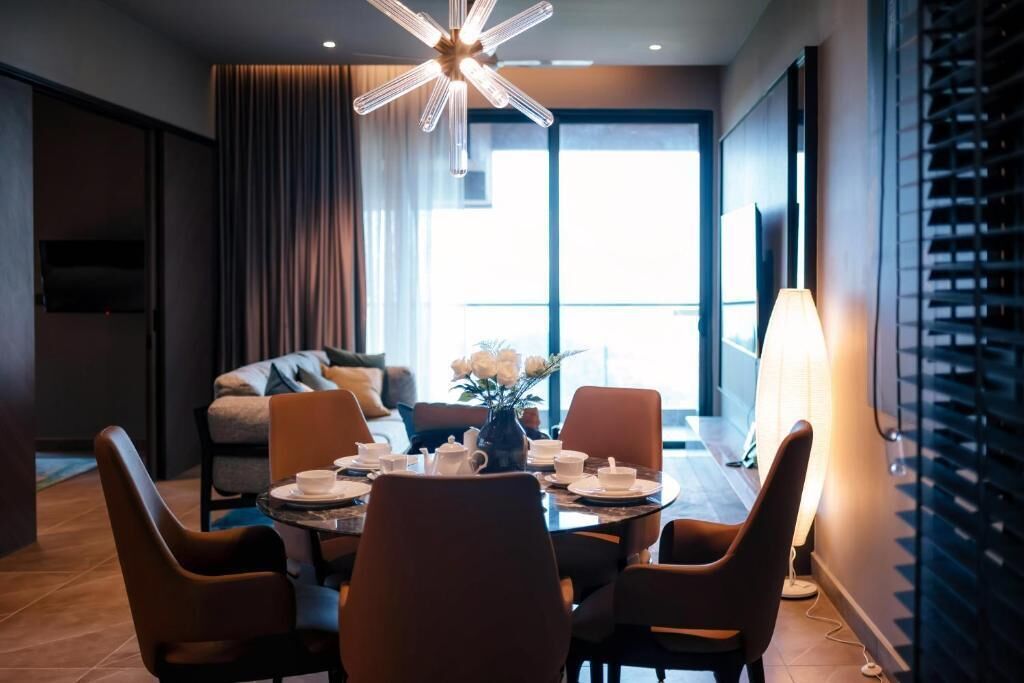 Una habitación de hotel moderna con zona de comedor, sofá, televisor y un ventanal grande.