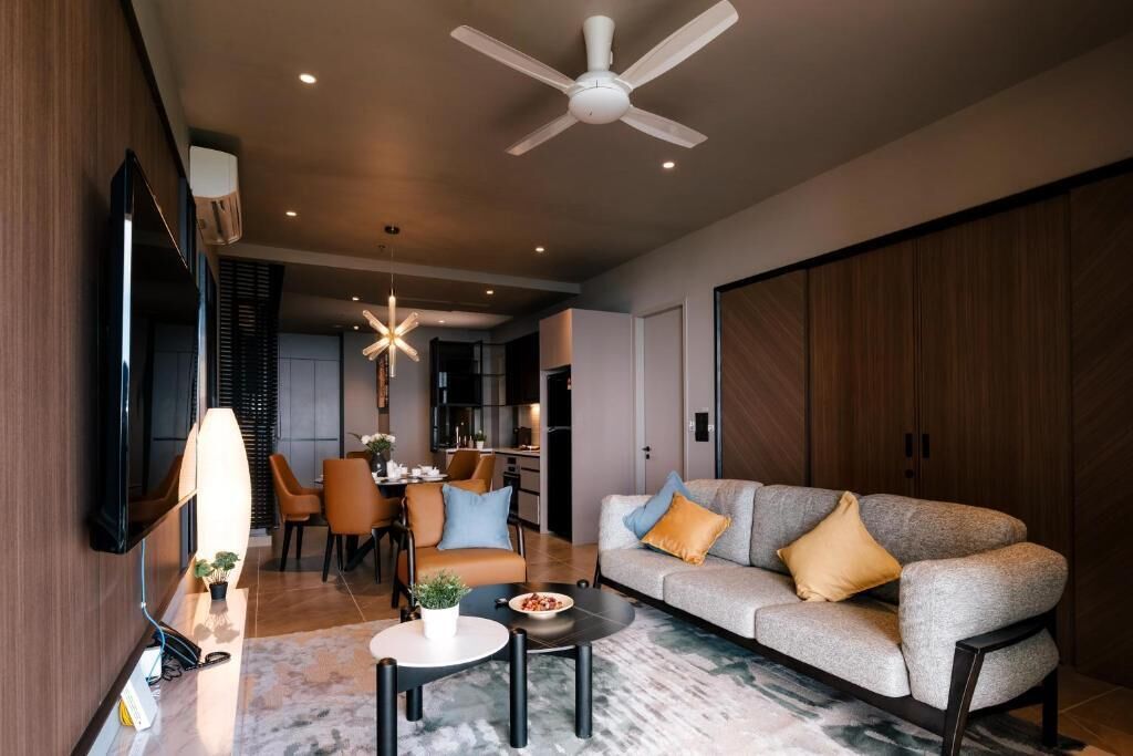 A modern living room with a sofa, coffee table, and TV. There is a dining area with chairs and a table. The room has a ceiling fan and recessed lighting.