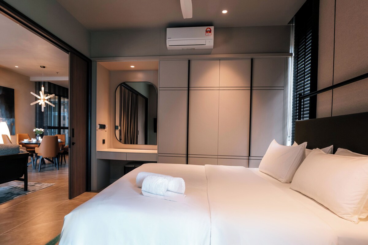 Una habitación de hotel con una cama grande, una mesita de noche, un espejo y un equipo de aire acondicionado.