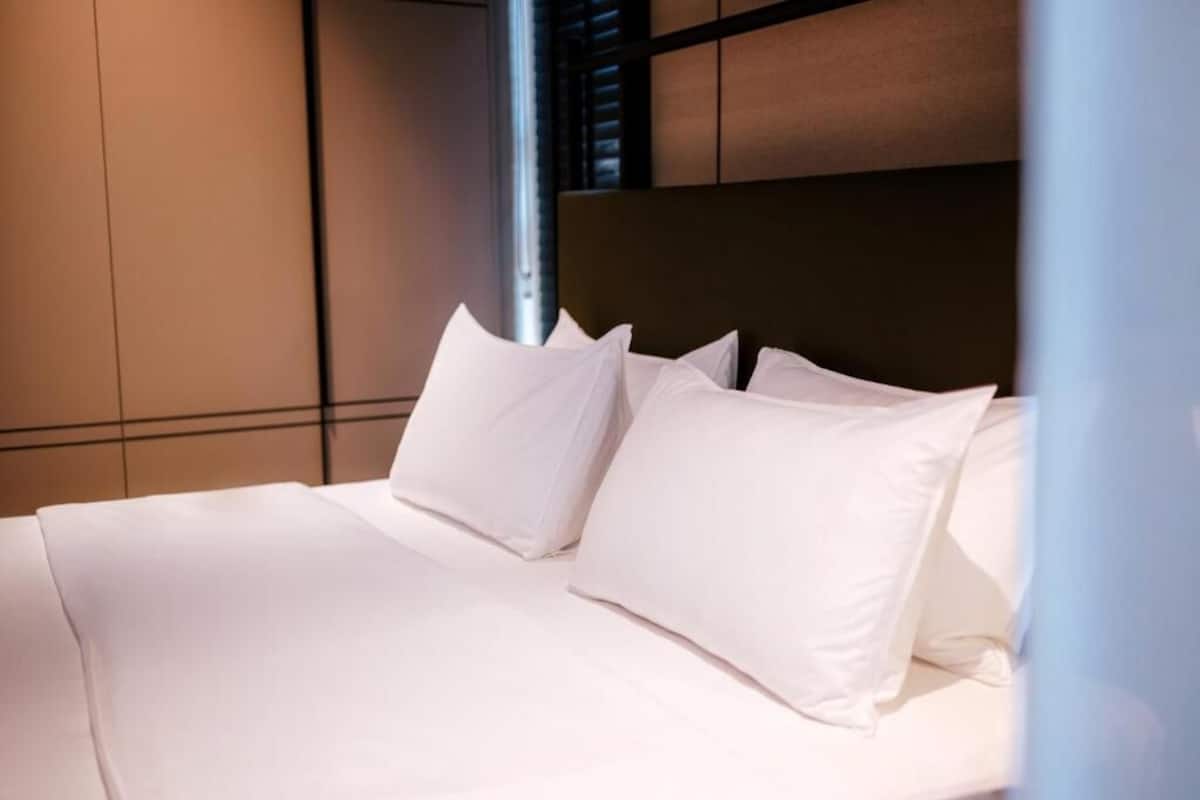 Una cama bien tendida con sábanas y almohadas blancas, un cabecero oscuro y un diseño moderno en la pared.