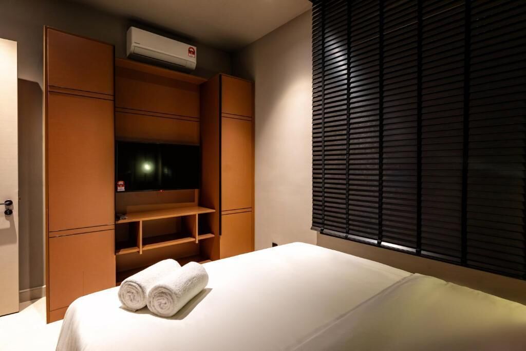 A hotel room with a bed, a TV, a wardrobe, and a window with blinds.