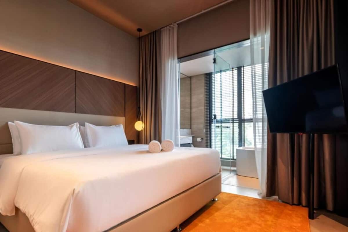 Una habitación de hotel moderna con una cama grande, un televisor de pantalla plana y una puerta de cristal que da a un balcón.