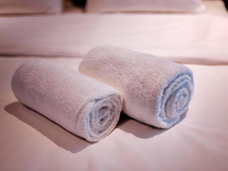 Two rolled towels on a bed with white linens.