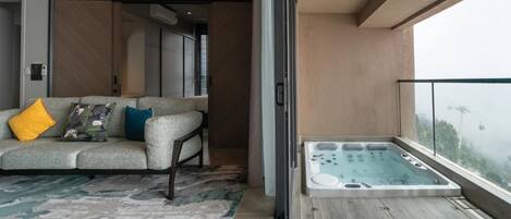 A modern living room with a sofa, a patterned rug, and a glass door leading to a balcony with a hot tub.