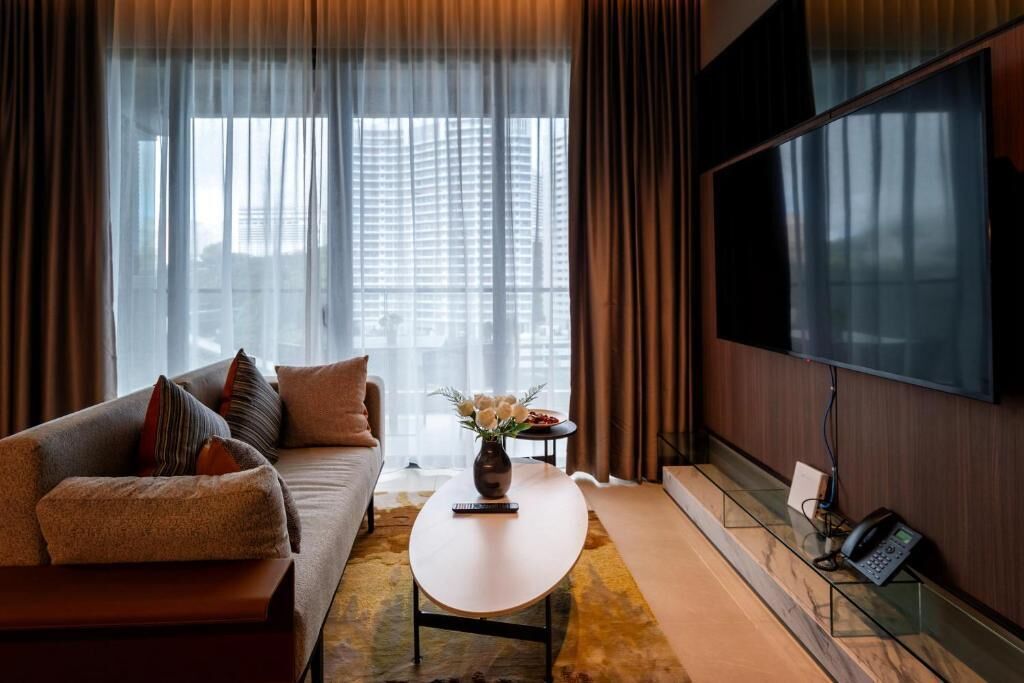 A modern living room with a sofa, a coffee table, a vase with flowers, a flat-screen TV, and a telephone.