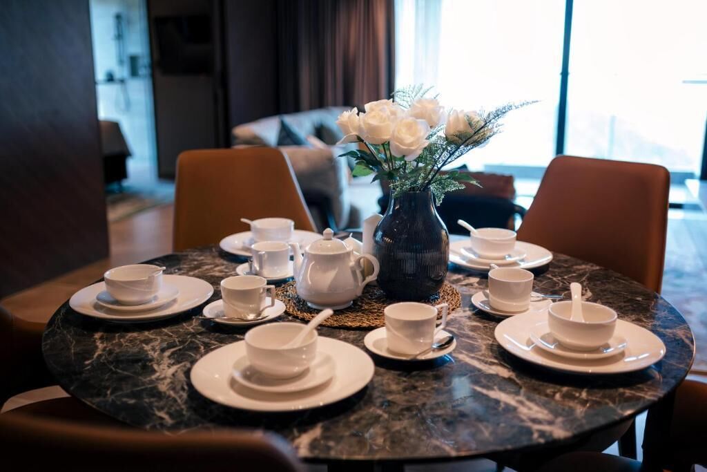 Una mesa de comedor dispuesta con tazas y platillos blancos, un florero con flores blancas y una superficie de mesa de mármol.