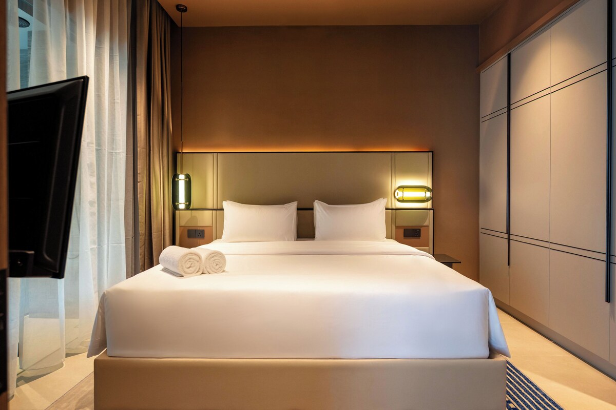 Habitación de hotel con una cama grande, dos mesitas de noche, un televisor de pantalla plana y un aplique de pared.