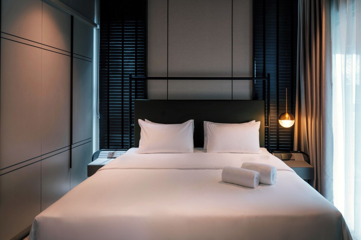 Una habitación de hotel moderna con una cama grande, mesitas de noche y una pequeña mesa auxiliar.