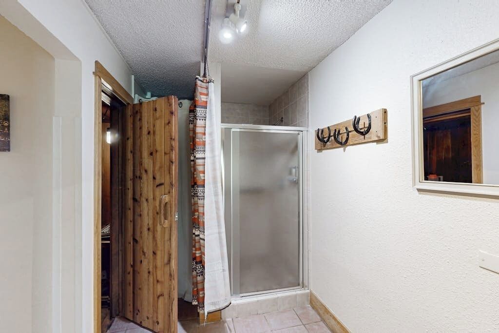 Una ducha con puerta de cristal, una puerta de madera parcialmente visible y un espejo instalado en la pared.