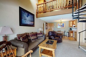 Ein Wohnzimmer mit einer Couch, einem Holztisch, einem Ledersessel, einer Treppe und einem Küchenbereich.