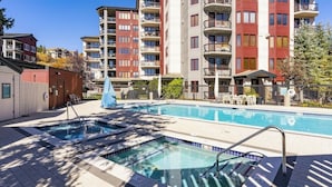 A swimming pool with a hot tub, surrounded by multi-story buildings with balconies. - Perfect Getaway with Mountain Views, Balcony, Shared Pool & Hot Tubs (Steamboat Springs)