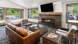 A modern living room with a fireplace, leather sofa, and a flat-screen TV. - Perfect Getaway with Mountain Views, Balcony, Shared Pool & Hot Tubs (Steamboat Springs)
