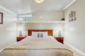 Ein Schlafzimmer mit einem großen Bett, zwei Nachttischen mit Lampen, einem Wanddekor und einem Fenster über dem Bett.