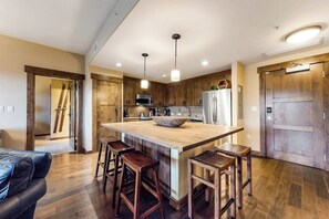 Eine moderne Küche mit einer zentralen Kochinsel, Barhocker, Holzschränken und einem Kühlschrank.