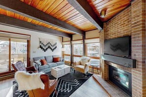 A modern living room with a fireplace, a large TV, and a cozy seating area. - Slopeside condo with pool, hot tubs, ski shuttle, fireplace, & deck (Steamboat Springs)