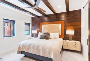 Ein modernes Schlafzimmer mit einem großen Bett, einem Holzkopfteil, Nachttischen und einem Fenster mit Jalousien.