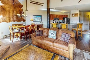 A living room with a brown leather sofa, wooden dining table, and chairs. - Third-floor condo with hot tub & pool, WiFi, fireplace & washer/dryer (Steamboat Springs)