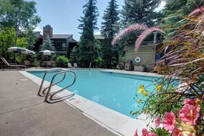 Ein Swimmingpool mit Metallleiter, umgeben von Bäumen und Sonnenschirmen.
