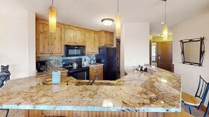 Eine Küche mit Holzausstattung, einer Granit-Arbeitsplatte, einer Spüle und zwei Pendelleuchten.