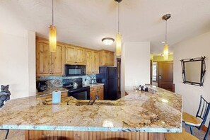 Eine Küche mit Holzausstattung, einer Granit-Arbeitsplatte, einer Spüle und zwei Pendelleuchten.