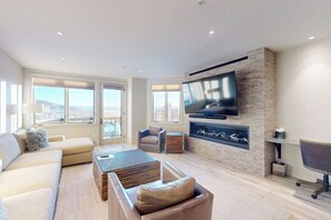 Ein modernes Wohnzimmer mit großem Flachbildfernseher, Kamin, Sofa, Couchtisch und Blick auf die Stadt durch große Fenster.