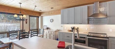 A modern kitchen with a large island, stainless steel appliances, and a wooden ceiling.