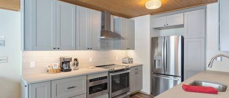 A modern kitchen with grey cabinets, stainless steel appliances, and a wooden ceiling.