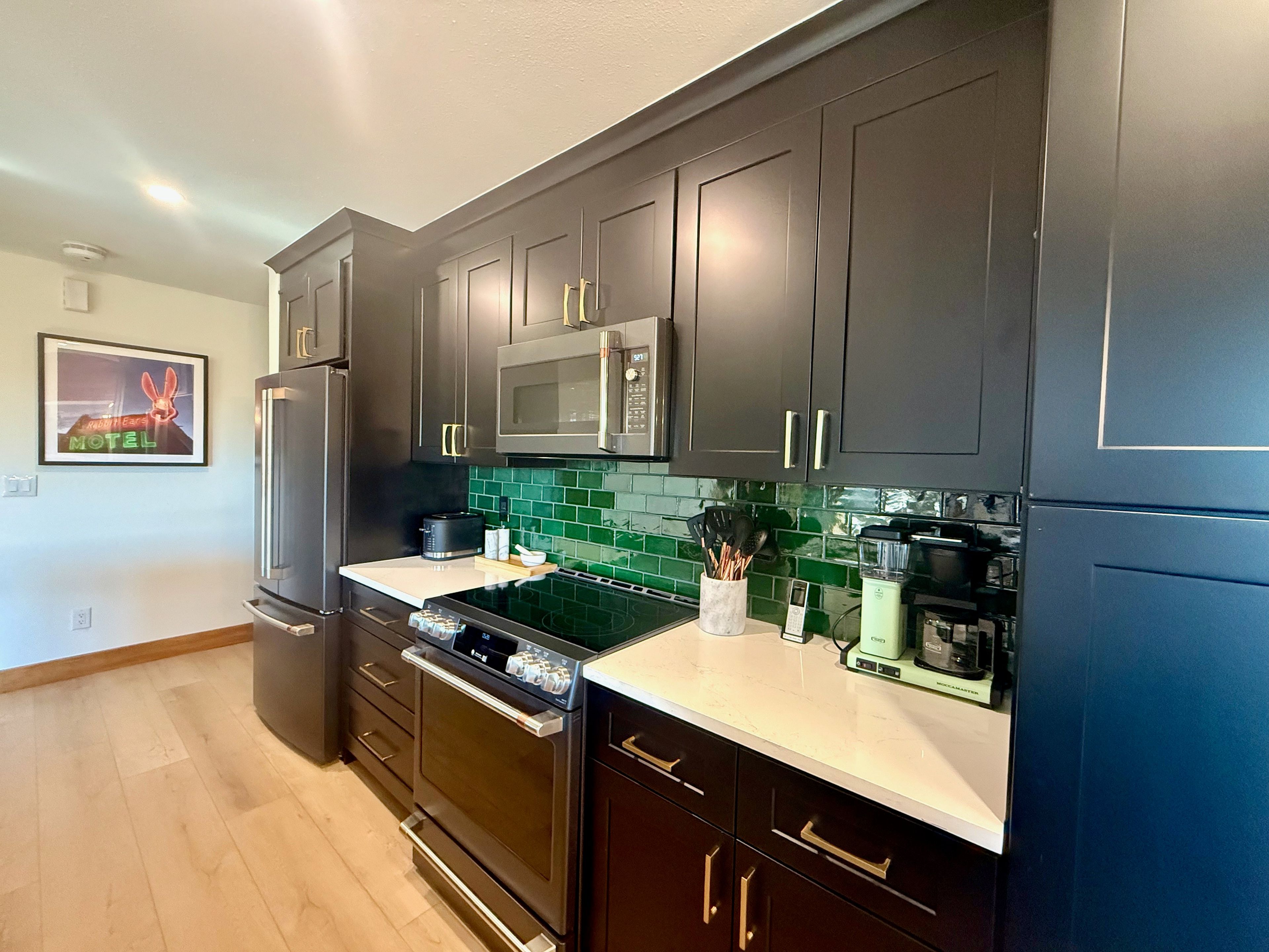 Uma cozinha moderna com armários escuros, eletrodomésticos de aço inoxidável e backsplash com azulejos verdes.