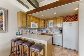 A kitchen with wooden cabinets, a white island with stools, a microwave, a refrigerator, and a dishwasher. - Amazing Ski-In/Out Condo w/Balcony, Free WiFi, Fireplace, Shared Hot Tub, Pool (Steamboat Springs)