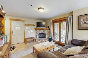 Ein gemütliches Wohnzimmer mit Kamin aus Stein, einem Fernseher, einer Couch und einem Holztisch.
