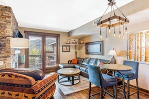 A living room with a stone wall, a sofa, a coffee table, and a TV. - Spacious mountain oasis w/ shared pool/hot tub, scenic balcony & high-speed WiFi (Steamboat Springs)