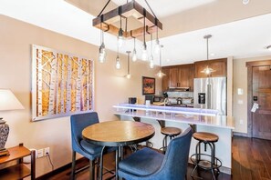 A modern kitchen with a central island, bar stools, and a dining table with chairs. - Spacious mountain oasis w/ shared pool/hot tub, scenic balcony & high-speed WiFi (Steamboat Springs)