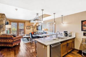 A modern kitchen with a central island, a dining area with a sofa, and a stone accent wall. - Spacious mountain oasis w/ shared pool/hot tub, scenic balcony & high-speed WiFi (Steamboat Springs)