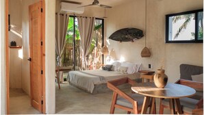 Une chambre à coucher avec un lit, un ventilateur de plafond, une fenêtre avec des rideaux, un téléviseur fixé au mur et une petite table sur laquelle est posé un vase.