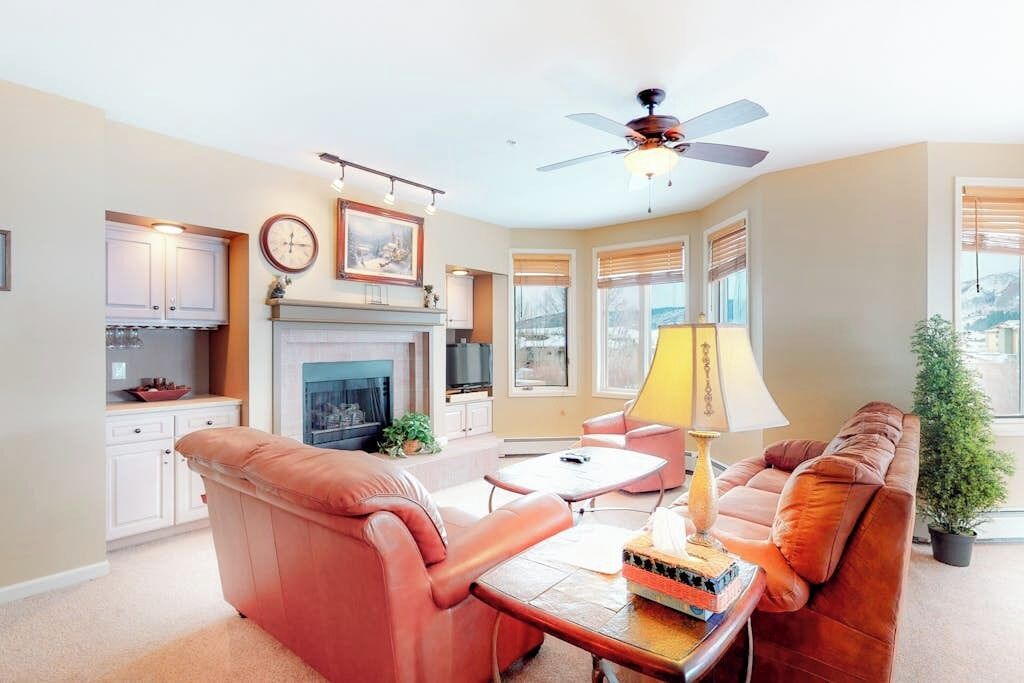 A living room with a fireplace, a ceiling fan, and a view of the outdoors.