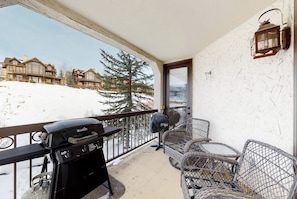 Ein Balkon mit Grill, Korbstühlen und Blick auf schneebedeckte Häuser.