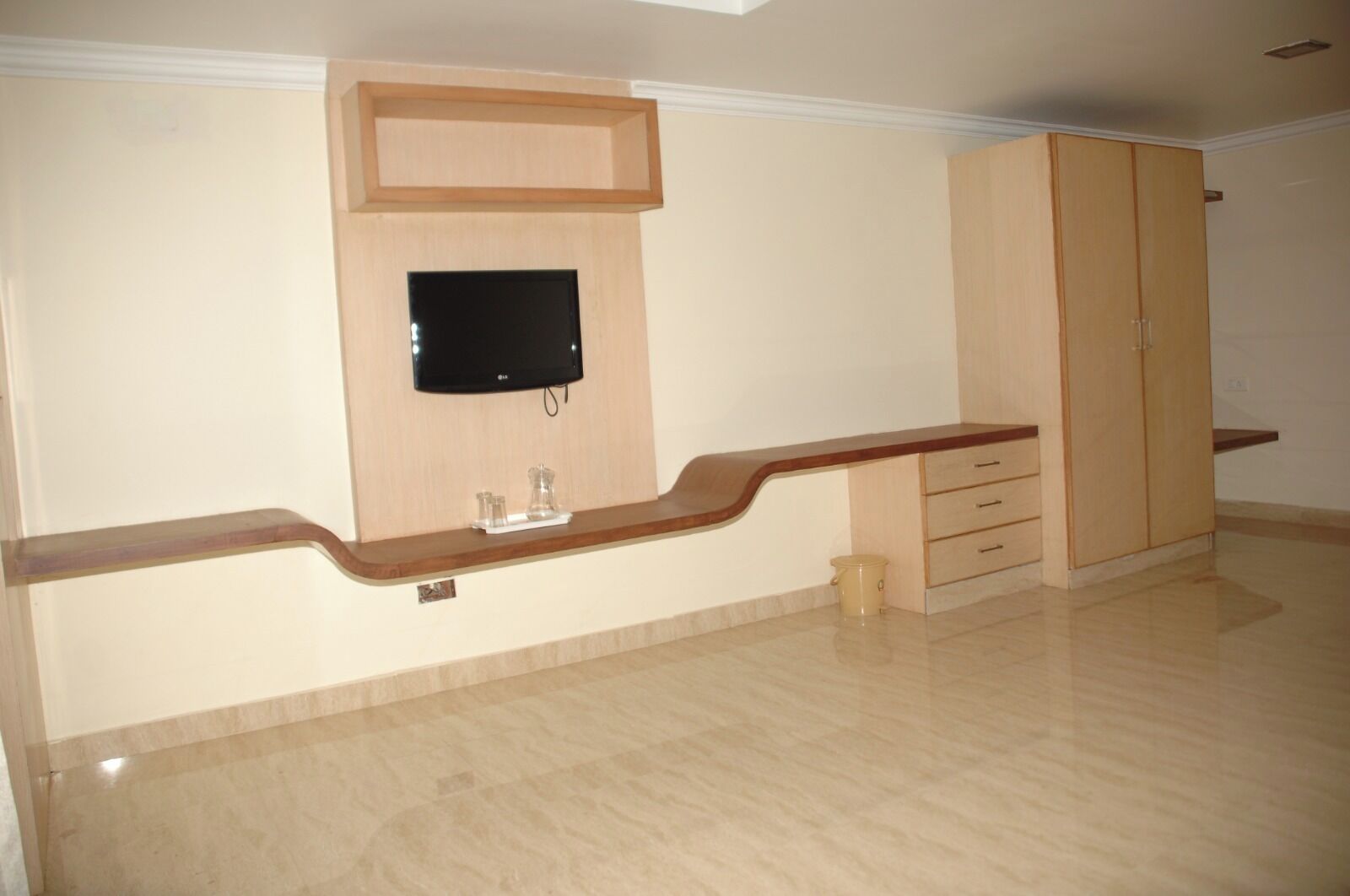 Una stanza con una TV a schermo piatto fissata a una parete in legno, un mobile contenitore in legno con cassetti e un pavimento piastrellato.