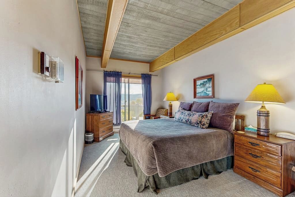 Une chambre à coucher avec un lit, des tables de chevet, une lampe, un tableau au mur et une fenêtre avec des rideaux.