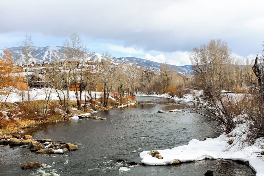 A river with snow-covered banks and mountains in the background.